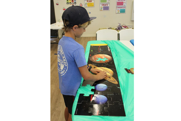a young boy putting together puzzle pieces of planets